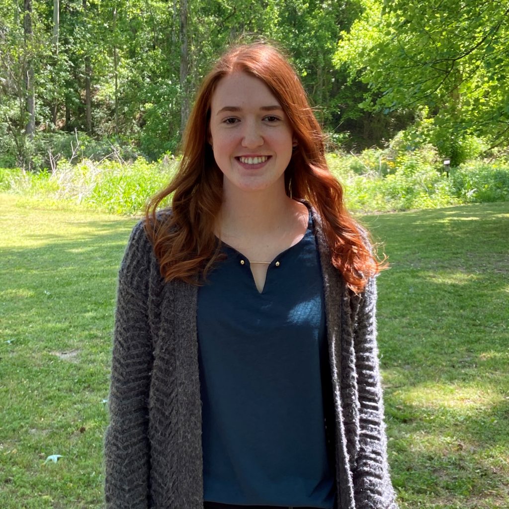 2021-22 Alabama Schweitzer Fellow Madison Hartley, standing in a field, wearing a dark-blue sweater and white blouse.