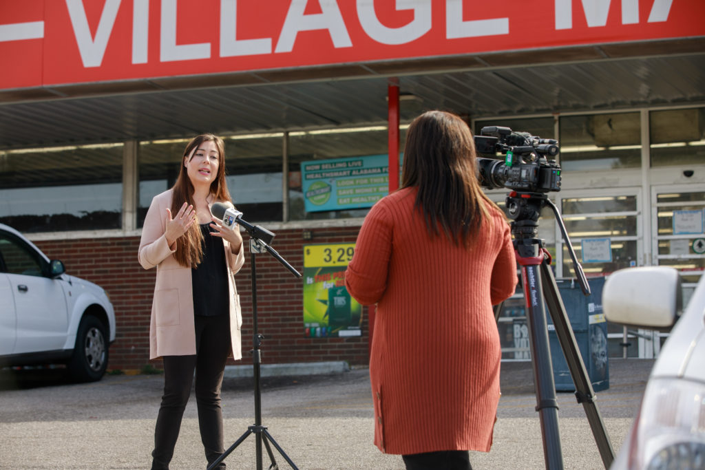 2020 ASF Fellow Katie Ellison speaking into a microphone in front of Village Market, located in the East Lake neighborhood of Birmingham.